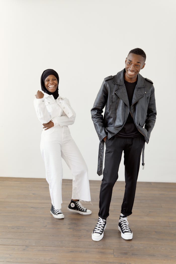 A joyful black Muslim couple in stylish outfits posing indoors with a bright background.